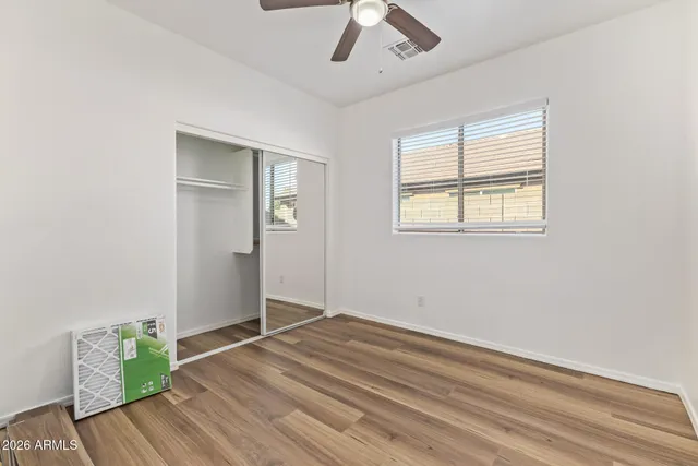 an empty room with wooden floor a ceiling fan and windows
