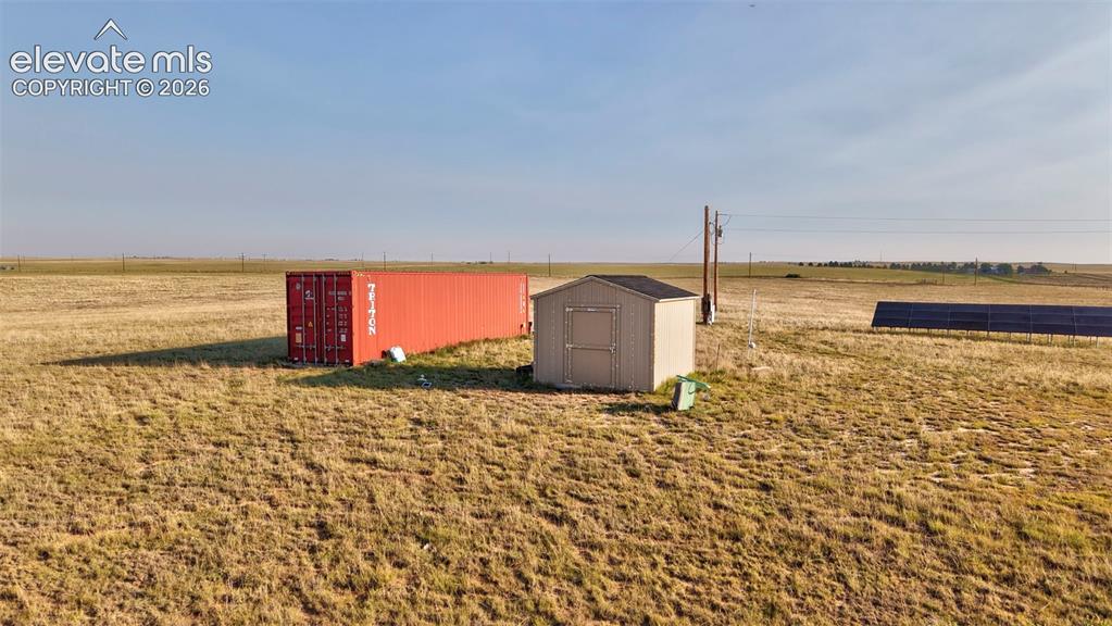 9670 Boone Road Yoder, CO 80864 - Photo 12 of 18 Expansive property featuring a red shipping container, a compact storage shed with a dark roof, and a ground-mounted solar panel array