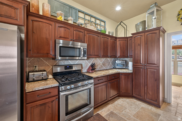 4635 East Sunny Acres Lane Moab, UT 84532 - Photo 46 of 56 Kitchen featuring rich wood cabinetry, stainless steel appliances, patterned tile backsplash, natural stone countertops, and tile flooring