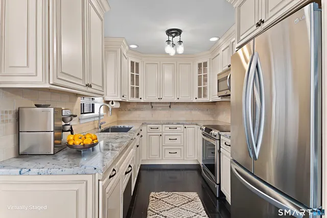 a kitchen with stainless steel appliances granite countertop a refrigerator a sink dishwasher a stove and white countertops with wooden floor