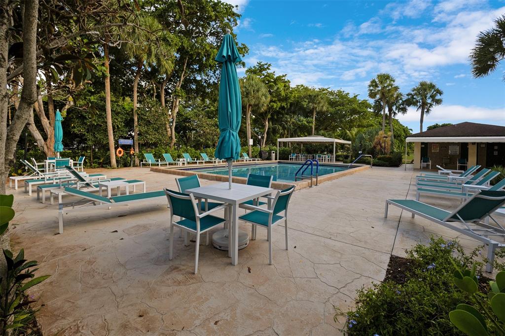 3095 North Course Drive, Unit 203 Pompano Beach, FL 33069 - Photo 47 of 49 a view of a patio with table and chairs under an umbrella with large trees