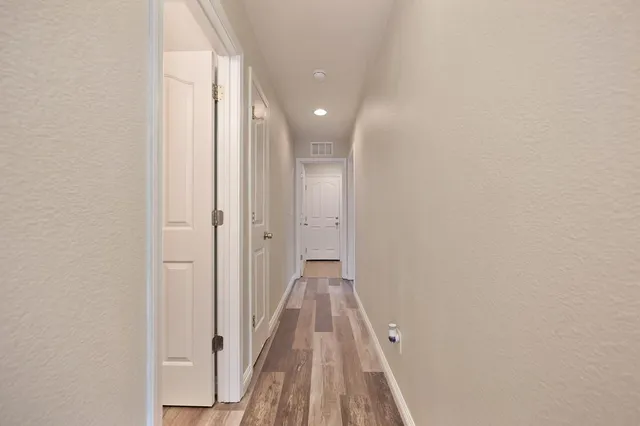 a view of a hallway with wooden floor and a bathroom