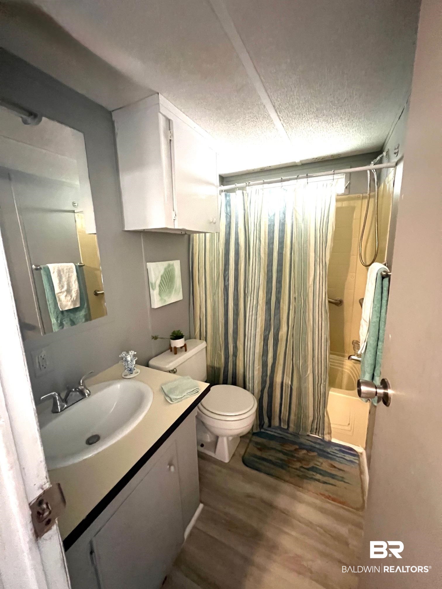 24994 Pompano Drive Elberta, AL 36530 - Photo 11 of 14 Full bath with a textured ceiling, vanity, wood finished floors, and shower / bathtub combination with curtain