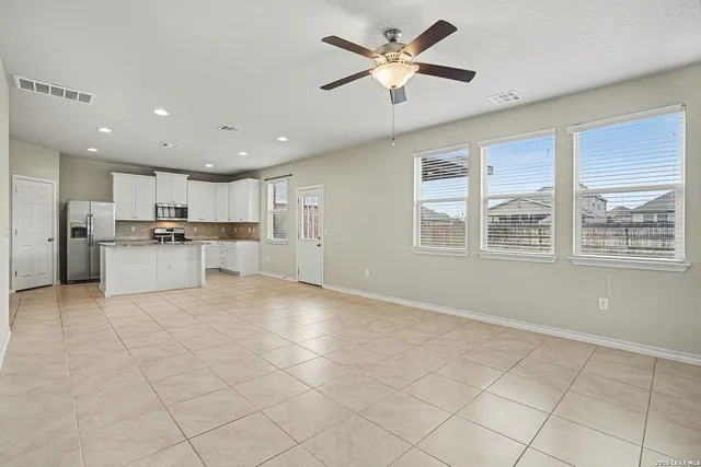a view of an empty room with kitchen appliances and a ceiling fan