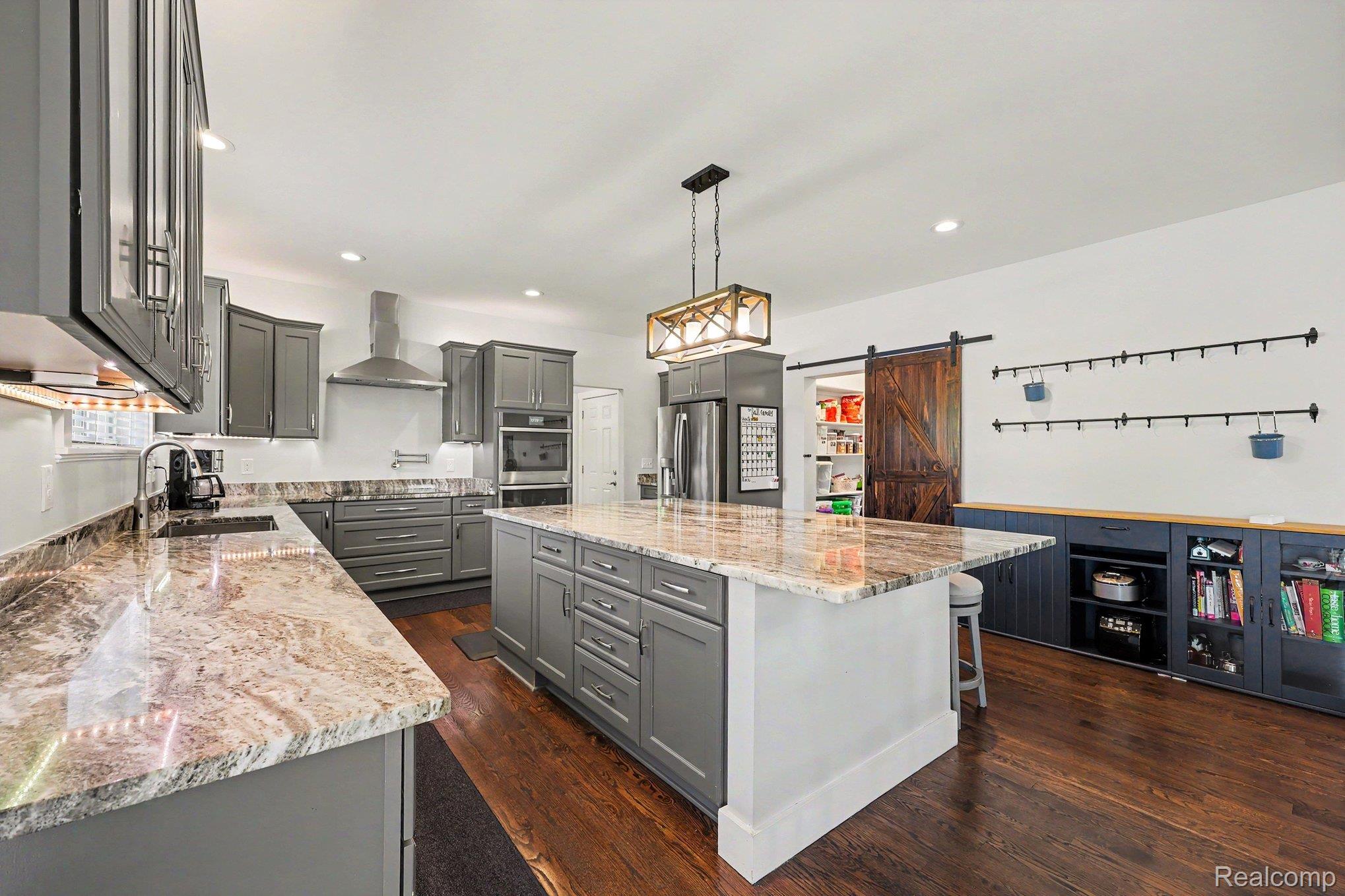 1660 Winthrop Road Bloomfield Hills, MI 48302 - Photo 10 of 38 Expansive kitchen featuring a large central island with seating, dark wood-finish flooring, grey cabinetry, stainless steel appliances, and light-toned countertops