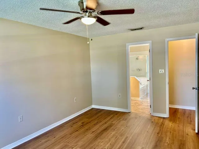 an empty room with wooden floor fan and windows