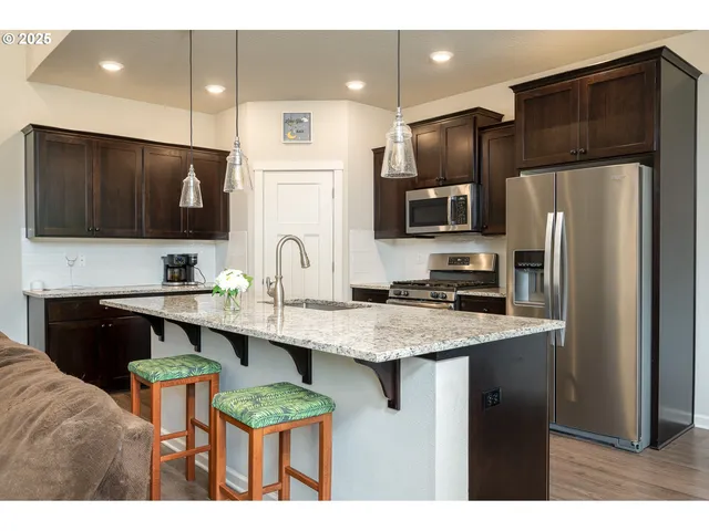 a kitchen with stainless steel appliances kitchen island granite countertop a refrigerator a sink a stove a microwave and wooden cabinets