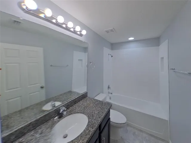 a bathroom with a granite countertop sink a toilet a mirror and shower