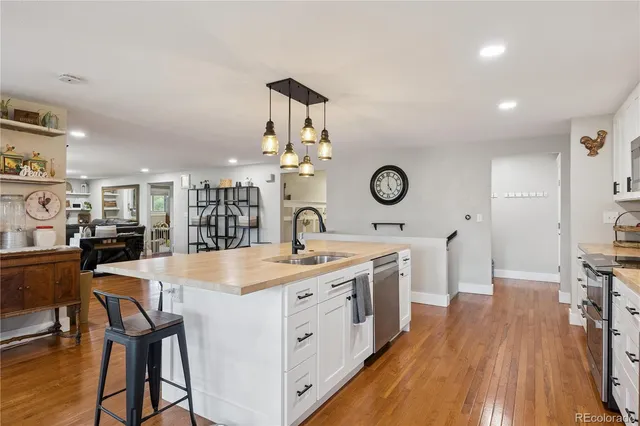 a large white kitchen with a stove a sink dishwasher and a dining table with wooden floor