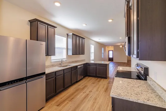 a large kitchen with stainless steel appliances granite countertop a refrigerator a sink dishwasher a stove and white countertops with wooden floor