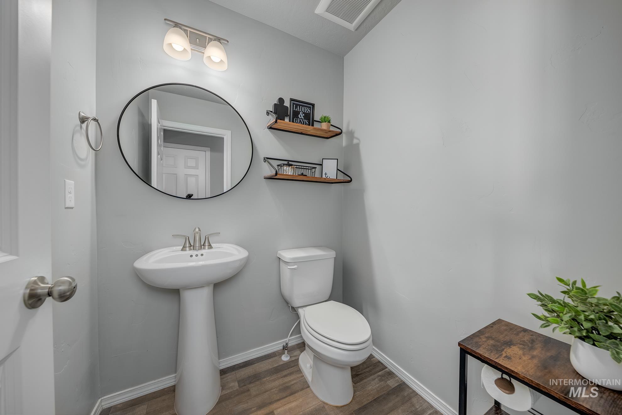 1049 Price Road Weiser, ID 83672 - Photo 12 of 47 Pedestal sink with a circular mirror, brushed nickel light fixture, toilet, wood-finish flooring, and light gray walls