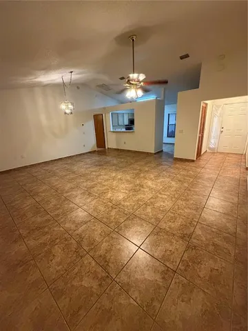 an empty room with a chandelier fan and kitchen view