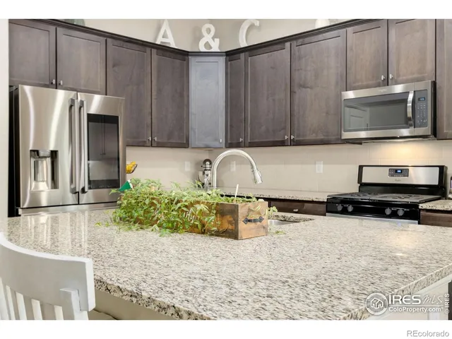 a open kitchen with stainless steel appliances kitchen island granite countertop a refrigerator a stove a dining table and chairs with wooden floor