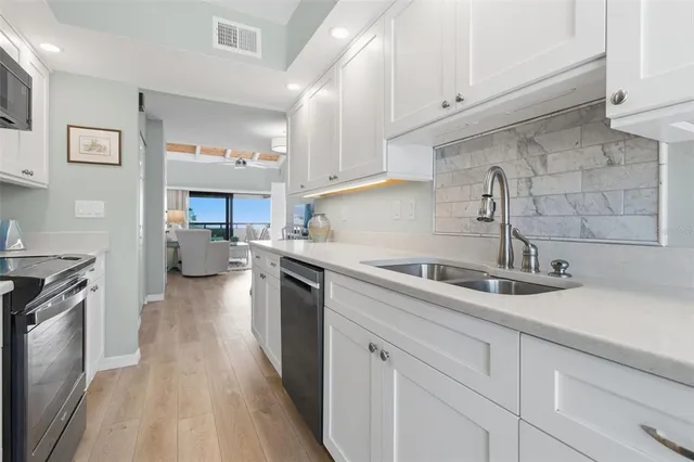 a kitchen with a sink dishwasher a stove and white cabinets with wooden floor