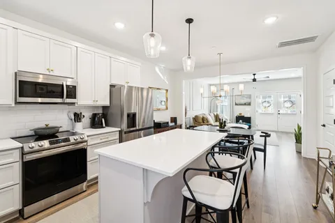 a kitchen with stainless steel appliances a stove a refrigerator a kitchen island a table and chairs