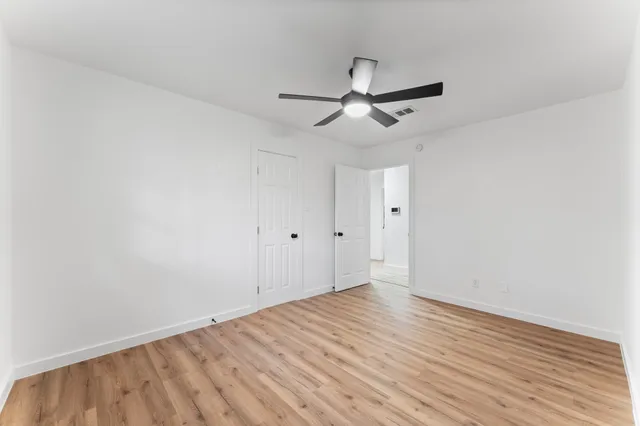an empty room with wooden floor a ceiling fan and windows