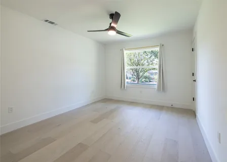 an empty room with wooden floor ceiling fan and windows