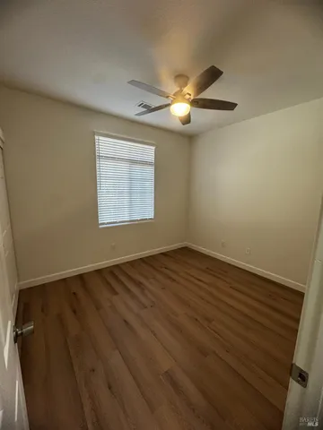 an empty room with wooden floor fan and windows