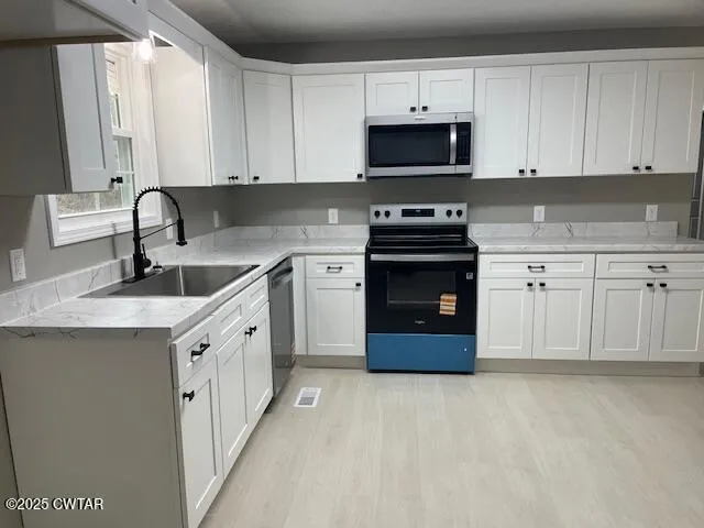 a kitchen with stainless steel appliances granite countertop a sink dishwasher a refrigerator with white cabinets and wooden floor