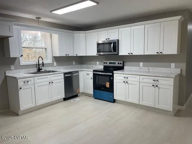 a kitchen with stainless steel appliances granite countertop a stove top oven a sink and white cabinets