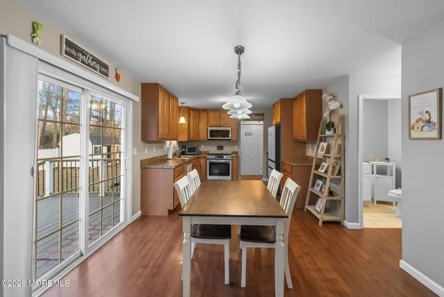 a dining room with stainless steel appliances kitchen island granite countertop a refrigerator a stove a microwave oven a dining table and chairs with wooden floor