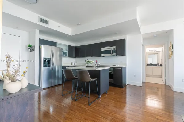 a kitchen with stainless steel appliances kitchen island granite countertop a refrigerator a stove a sink a dining table and chairs with wooden floor