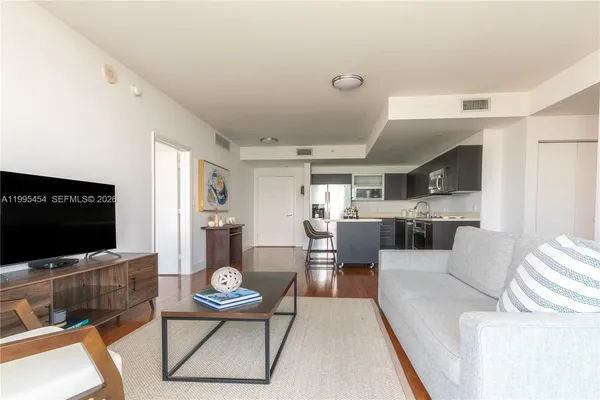 a living room with furniture a flat screen tv and kitchen view