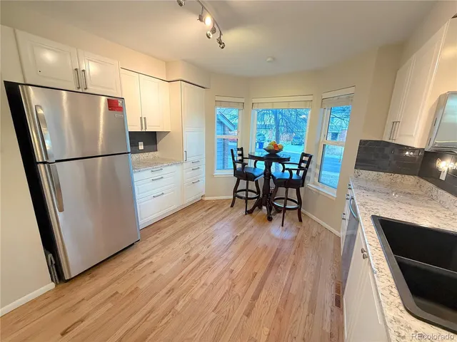 a kitchen with stainless steel appliances granite countertop a refrigerator stove a dining table and chairs with wooden floor