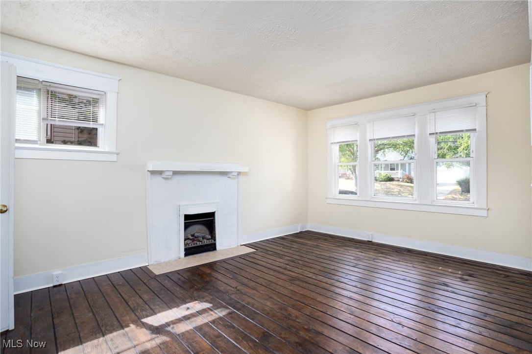 555 Brittain Road Akron, OH 44305 - Photo 16 of 26 Unfurnished living room featuring dark wood-style floors, a fireplace with flush hearth, and a textured ceiling