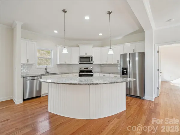 a kitchen with stainless steel appliances granite countertop a sink a stove a refrigerator and island with wooden floor