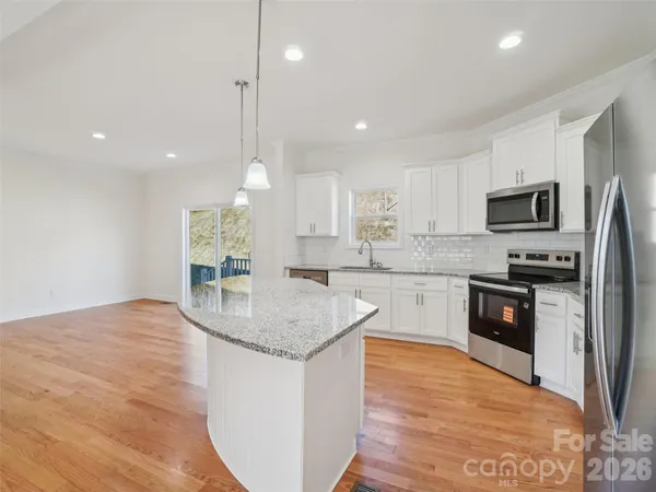 a kitchen with stainless steel appliances granite countertop a sink a stove a refrigerator and white cabinets with wooden floor