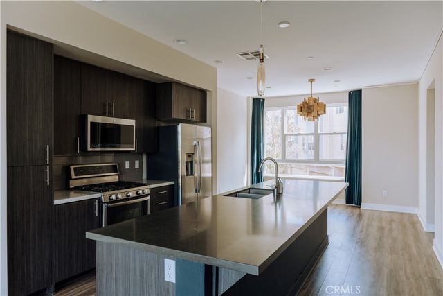 a kitchen with stainless steel appliances granite countertop a refrigerator a stove and a sink with wooden floor