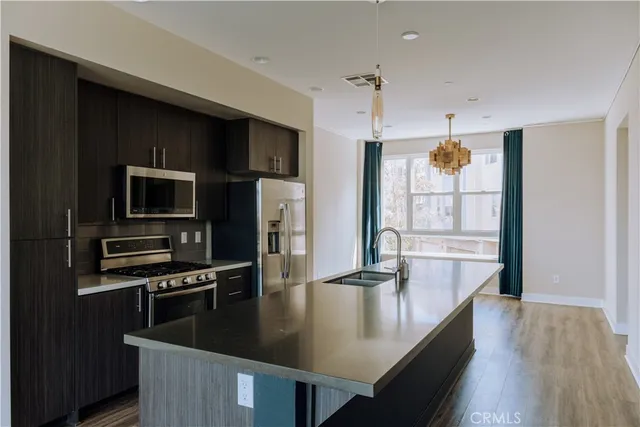 a kitchen with stainless steel appliances granite countertop a refrigerator a stove and a sink with wooden floor