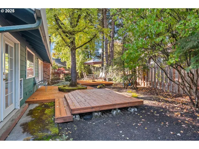 a view of a patio with table and chairs with wooden fence and large trees