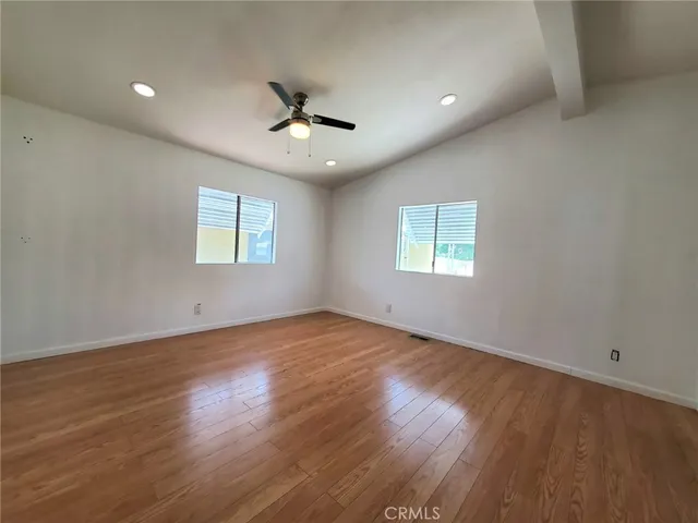 an empty room with wooden floor ceiling fan and window