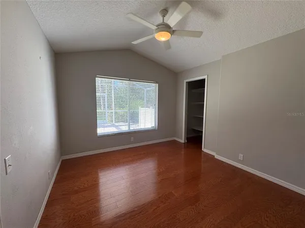 an empty room with wooden floor chandelier fan and windows