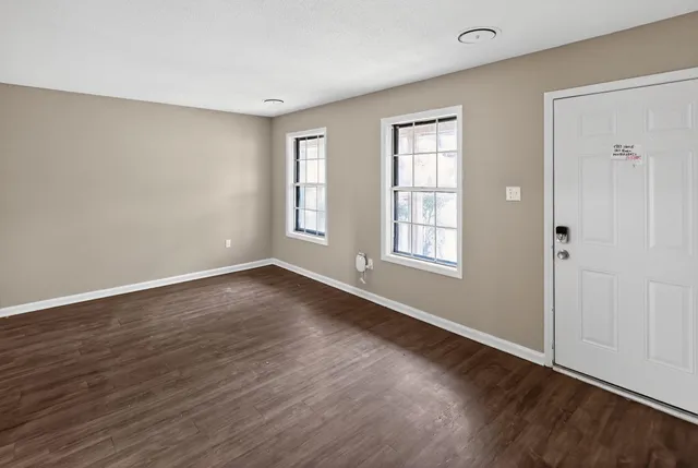 a view of an empty room with wooden floor and a window