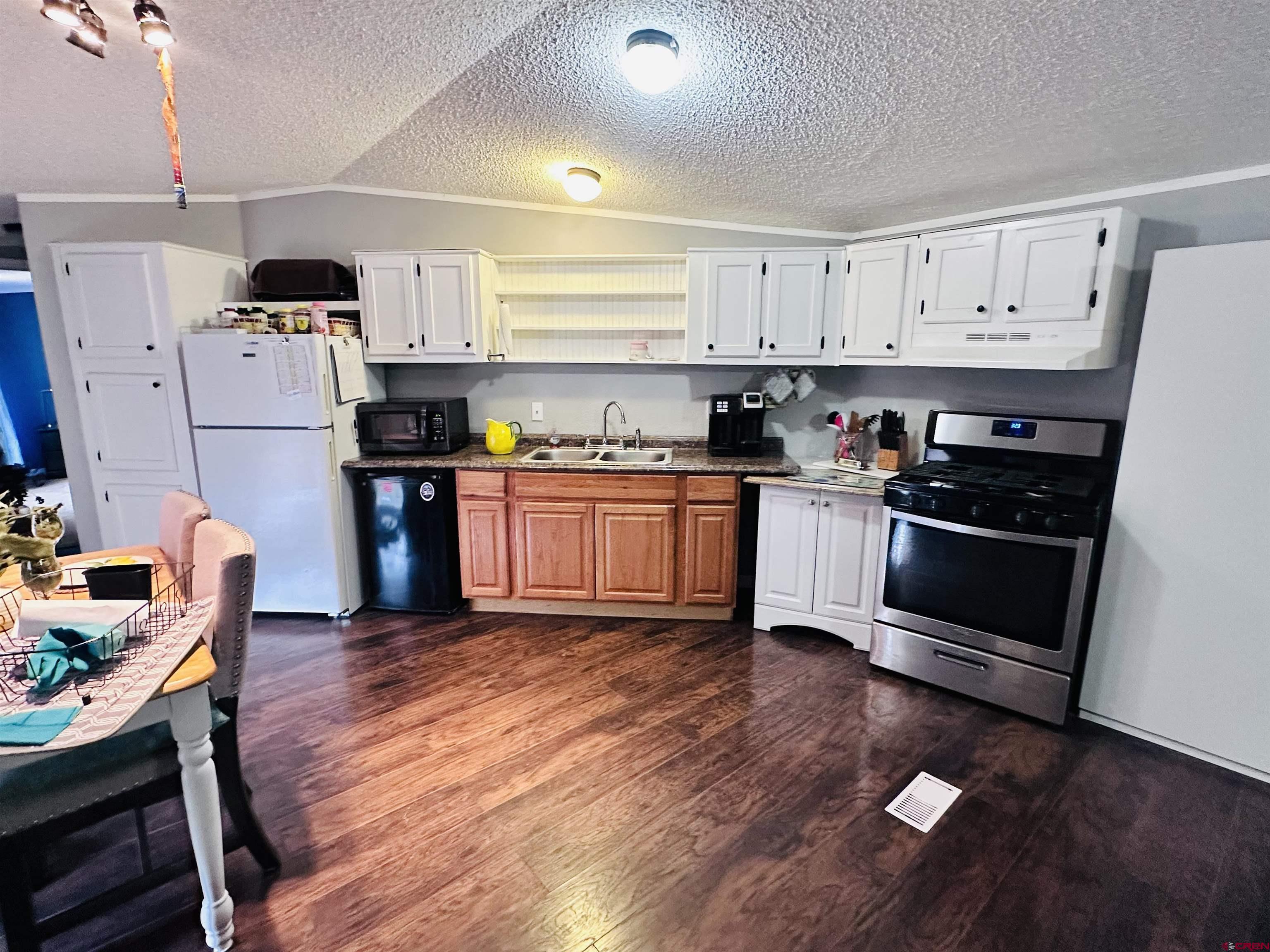 62880 Lasalle Road, Unit 174 Montrose, CO 81401 - Photo 11 of 23 a kitchen with granite countertop a stove top oven a sink dishwasher and white cabinets with wooden floor