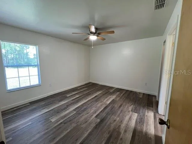 an empty room with wooden floor ceiling fan and windows