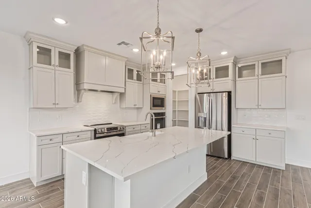 a kitchen with stainless steel appliances kitchen island granite countertop a refrigerator a sink dishwasher and white cabinets with wooden floor