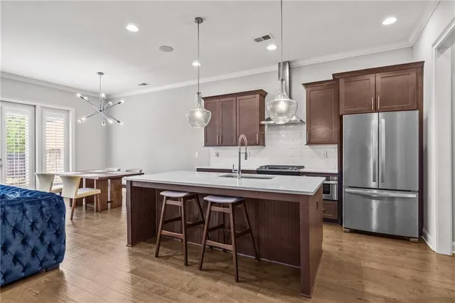 a kitchen with stainless steel appliances granite countertop a kitchen island a stove a refrigerator a sink a dining table and chairs with wooden floor