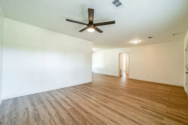 an empty room with wooden floor ceiling fan and windows