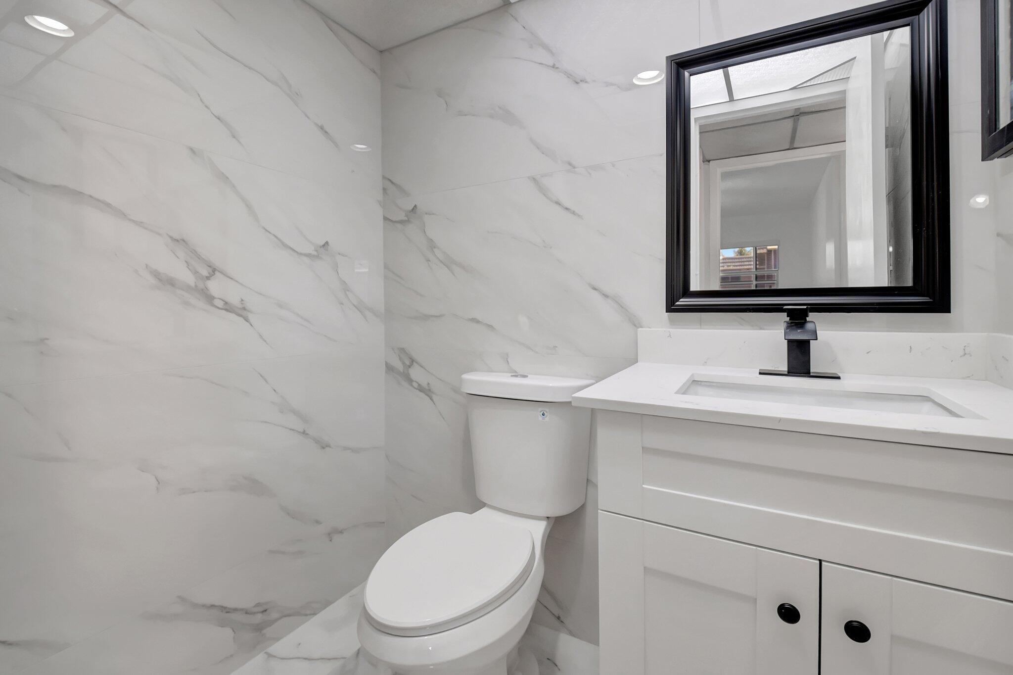 21 Brittany F, Unit A Delray Beach, FL 33446 - Photo 12 of 41 a bathroom with a toilet sink vanity and mirror
