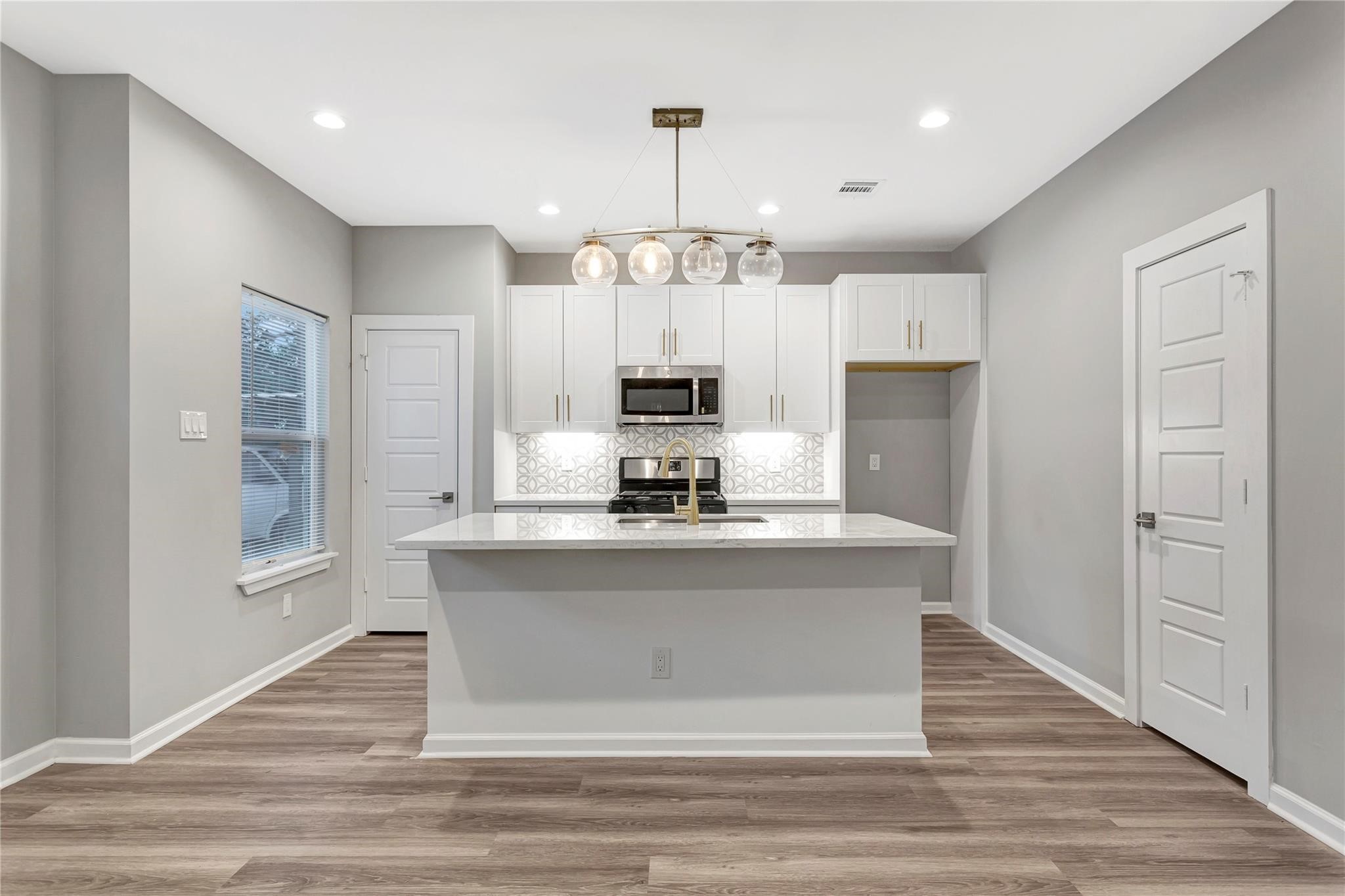 6813 Liverpool Street, Unit B Houston, TX 77021 - Photo 3 of 9 White shaker cabinets, quartz island, gold fixtures, gas range, stainless appliances, and geometric tile backsplash with globe pendant lighting