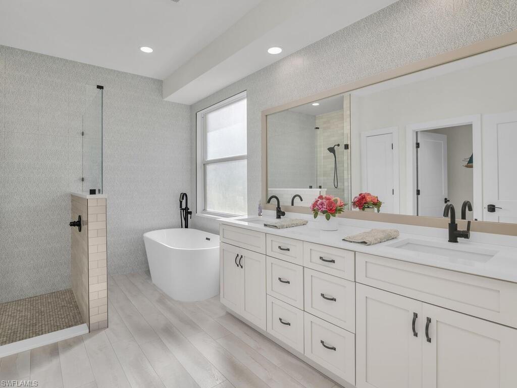 8541 Peppertree Way Naples, FL 34114 - Photo 12 of 36 Primary Bathroom featuring double vanity, large shower with freestanding bathtub, custom tile, and vinyl wood-style flooring