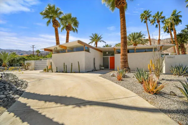 a palm tree sitting in front of a house with wooden fence