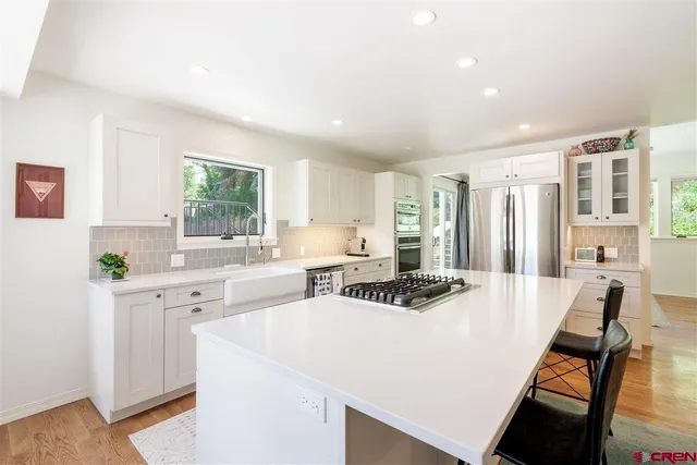 a kitchen with stainless steel appliances a stove a sink a refrigerator white cabinets and couches with wooden floor