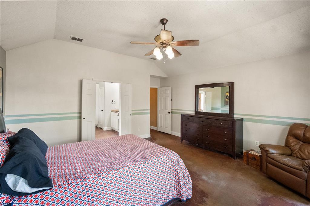 1305 Liverpool Lane Mansfield, TX 76063 - Photo 16 of 40 This bedroom features a vaulted ceiling with a ceiling fan, light-colored walls with a decorative accent stripe, and a doorway leading to a vanity area