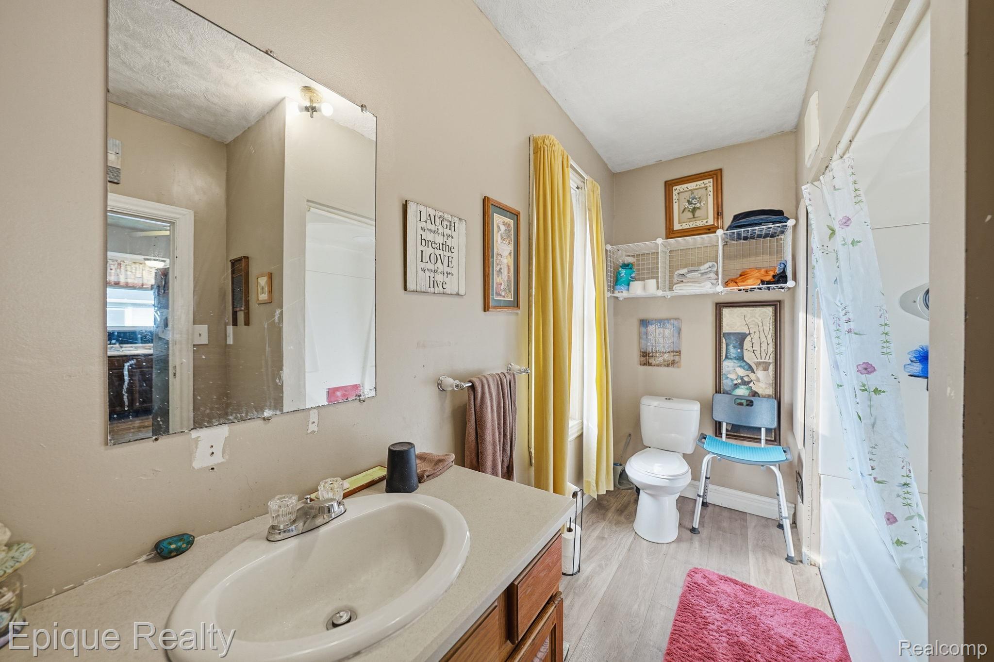 75 East Cicotte Street River Rouge, MI 48218 - Photo 15 of 25 Bathroom featuring a vanity with a white oval sink and chrome faucet, a wall-mounted mirror, a toilet, a window with yellow curtains, and wood-finish flooring