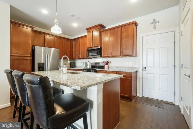 a kitchen with stainless steel appliances granite countertop a refrigerator a stove top oven a sink dishwasher and a dining table with wooden floor